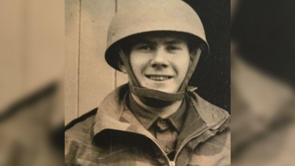 A sepia-tinted photo of Mr Gibbon, smiling, as a young man in Army uniform