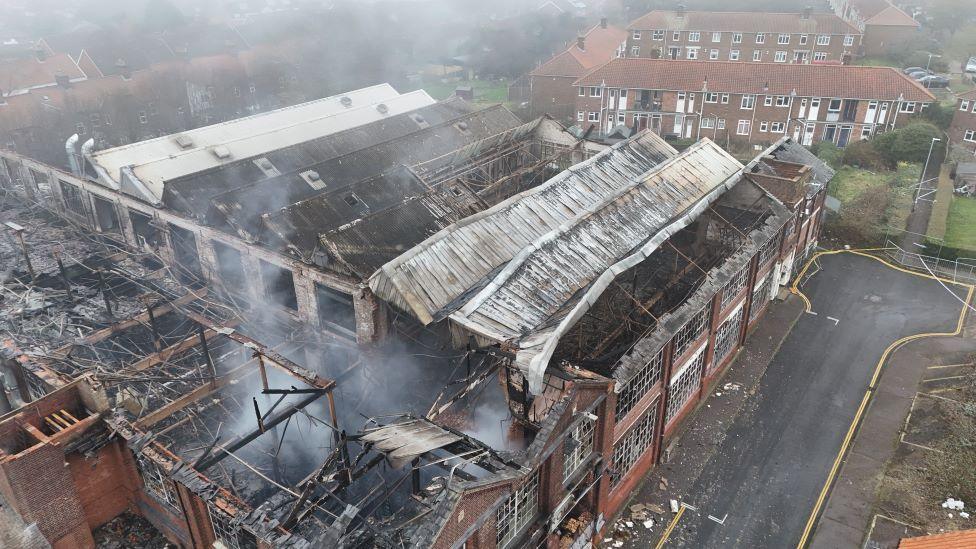 An aerial picture taken from above the derelict shoe factory on Dibden Road in Norwich. Smoke can still be seen coming off the building. Parts of the roof have collapsed and others are burnt and charred. 