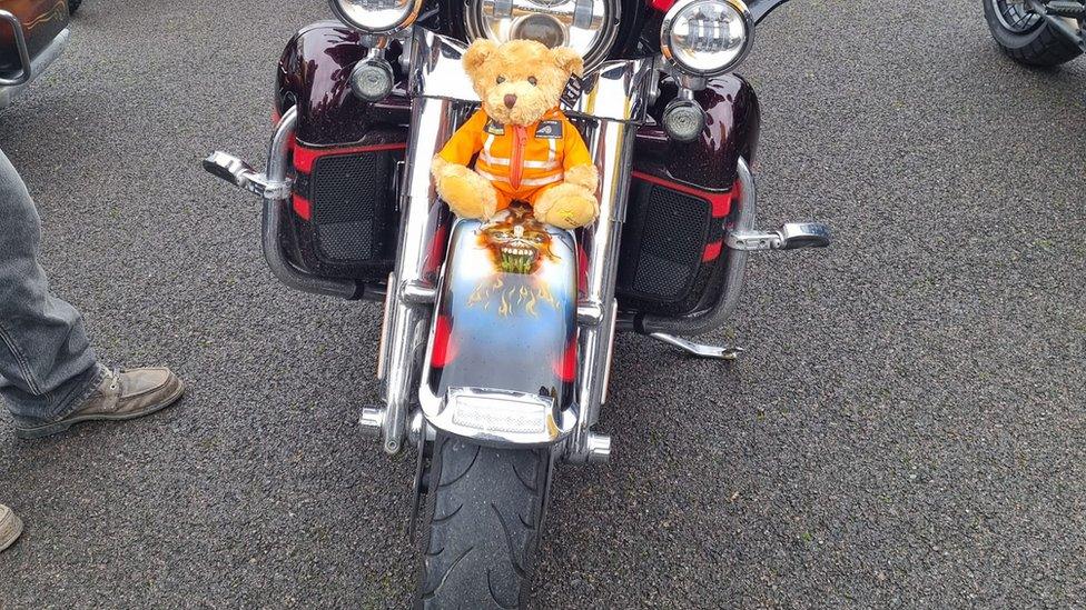 Front of motorbike showing an orange teddy bear sitting on the wheel