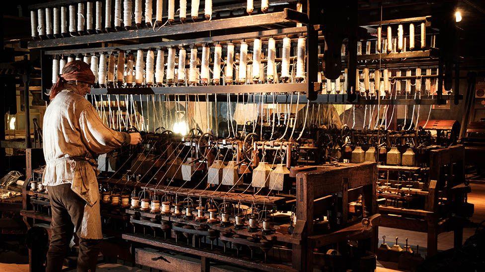 A man in period dress working on a huge machine spinning reels of cotton inside Helmshore Mills Textile Museum