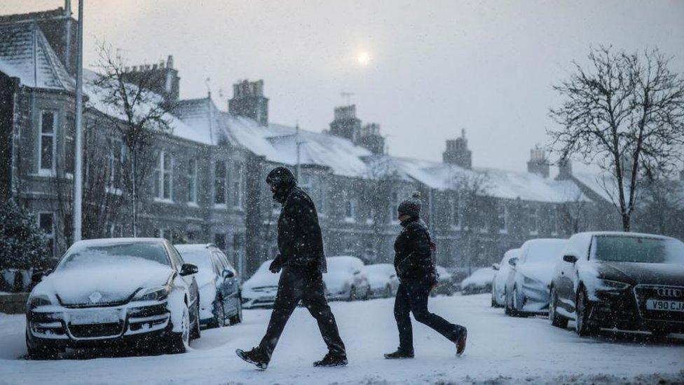 Two people walking across a road in the snow