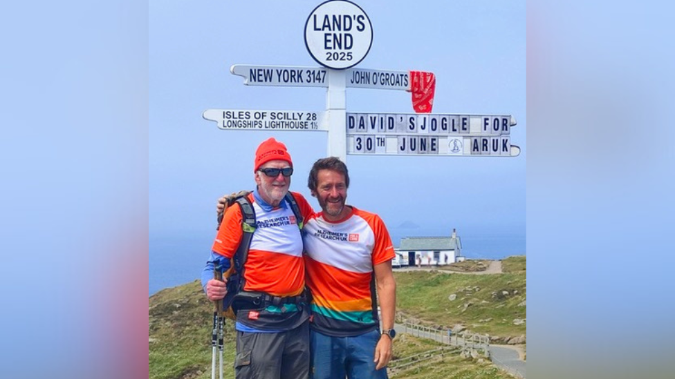 David Ensor, in full walking gear, with another man standing in front of the iconic white Land's End sign.