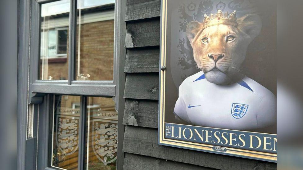 A framed picture of a Lion wearing a white England shirt attached to the outside of a pub.