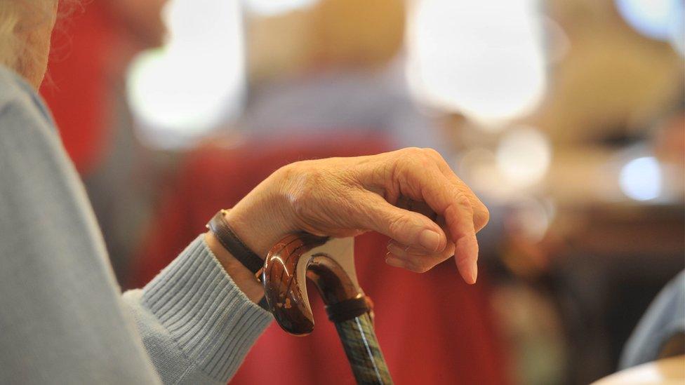 Elderly person sat down with walking stick in front of them