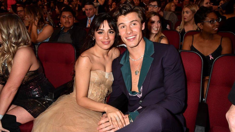 Camila Cabello and Shawn Mendes sit together smiling and holding hands