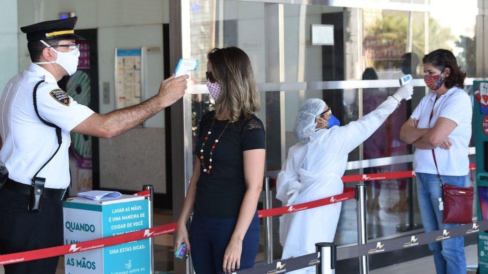 Workers check the body temperature of people before entering a shopping mall in Brasilia, Brazil, on May 27, 2020,