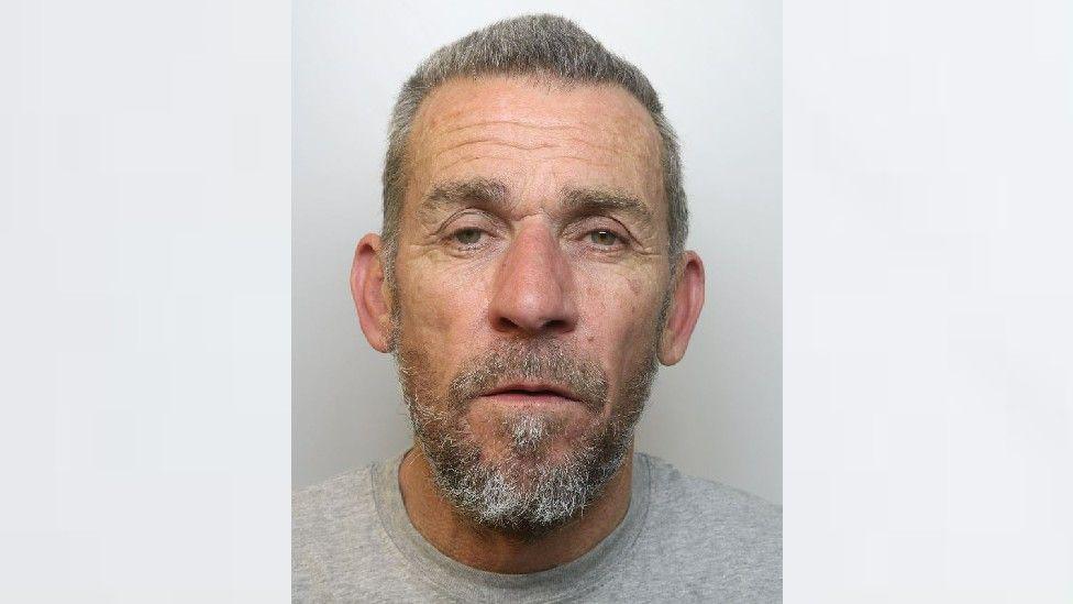 Police image of Gary John Selwood, with short grey hair, grey beard and grey t shirt.