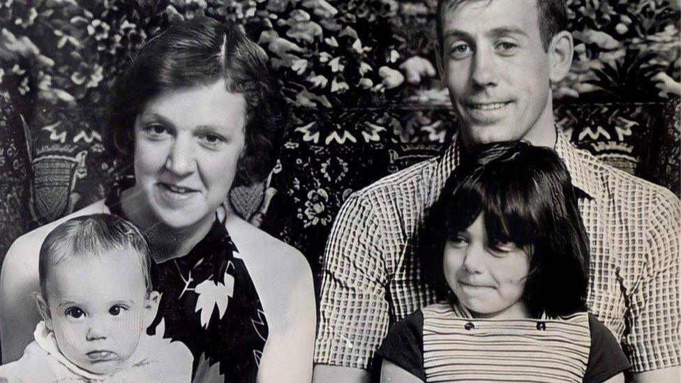 Old black and whitye photo of the Lee family. A woman and man sit next to each other. The woman has a young baby on her lap, the man has a toddler with shoulder length dark hair on his.