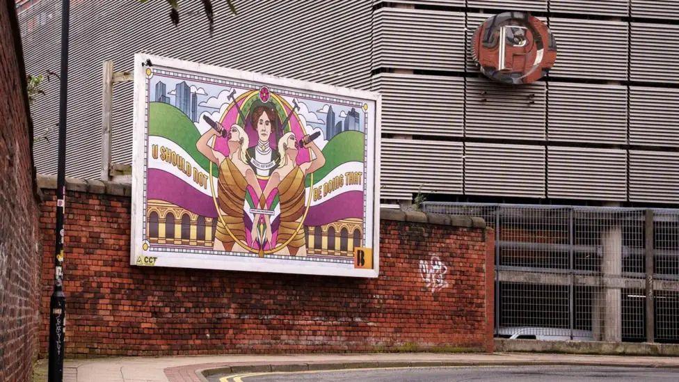 A billboard with a mural of two people singing with microphones above a brick wall in Manchester