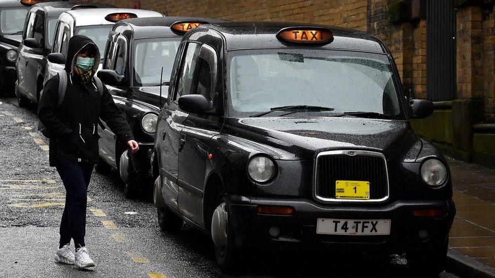 Person with face mask walks past line of taxis in Liverpool