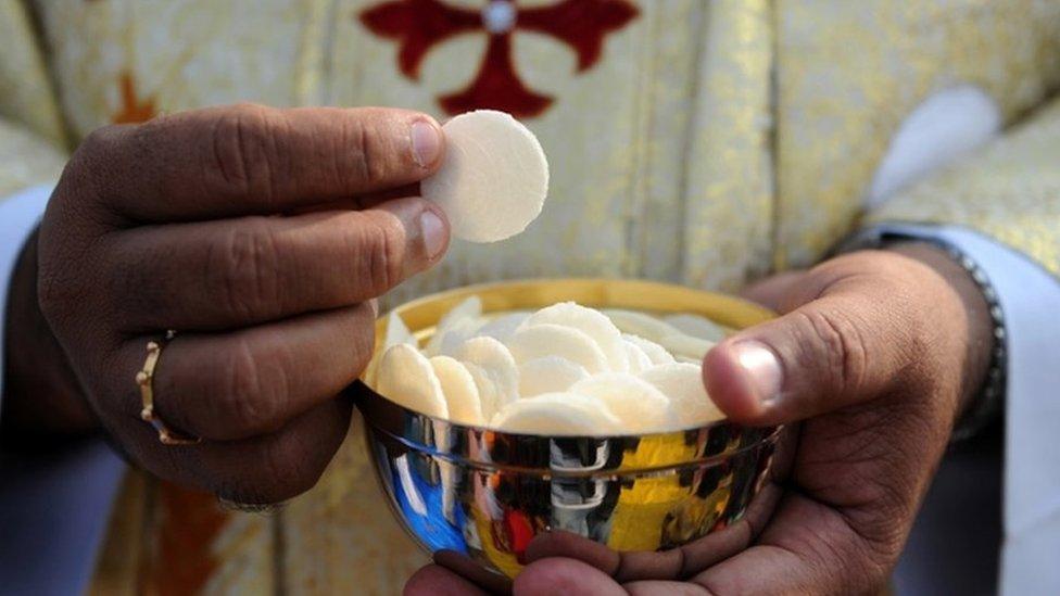 Priest holds a cup of wafers