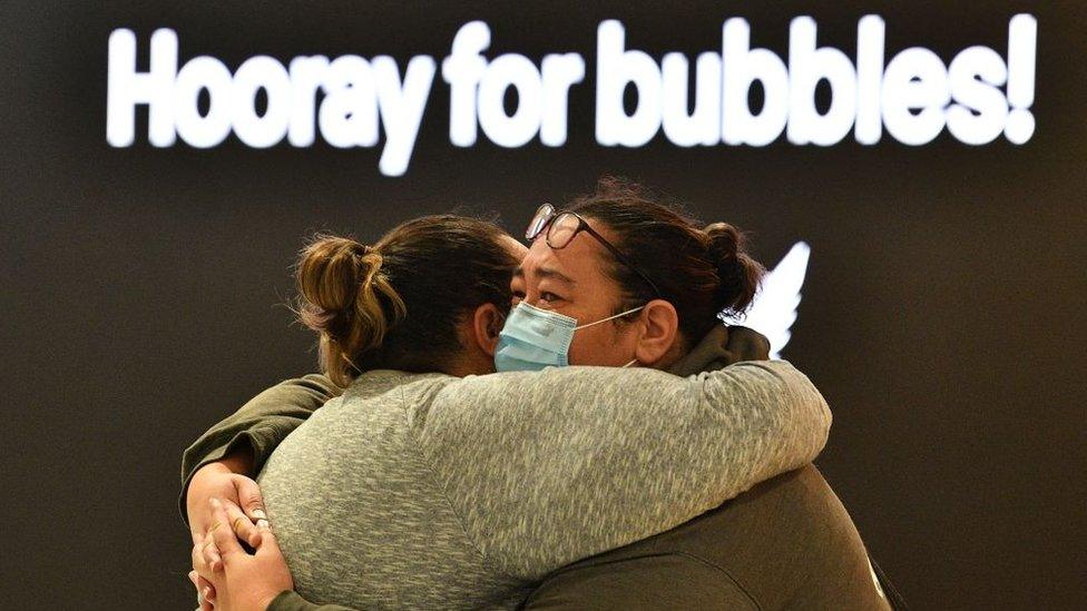 Two women hugging next a sign that reads "hooray for bubbles"