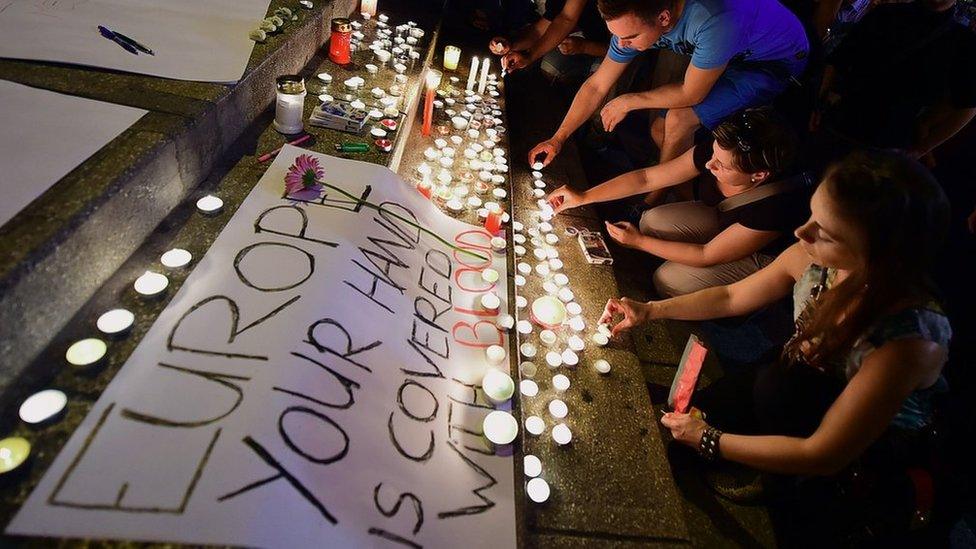 People light candles next to A banner reading "Europe, your hand is covered with blood" in front of a transit zone for migrants in Budapest