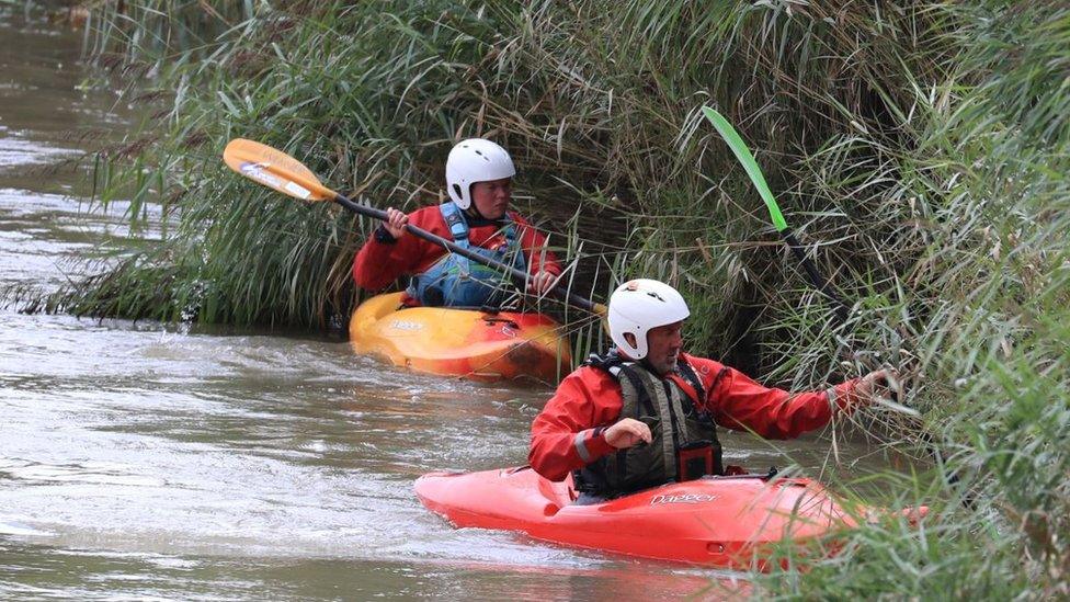 Search teams in canoes combing the dense vegetation on the riverbank