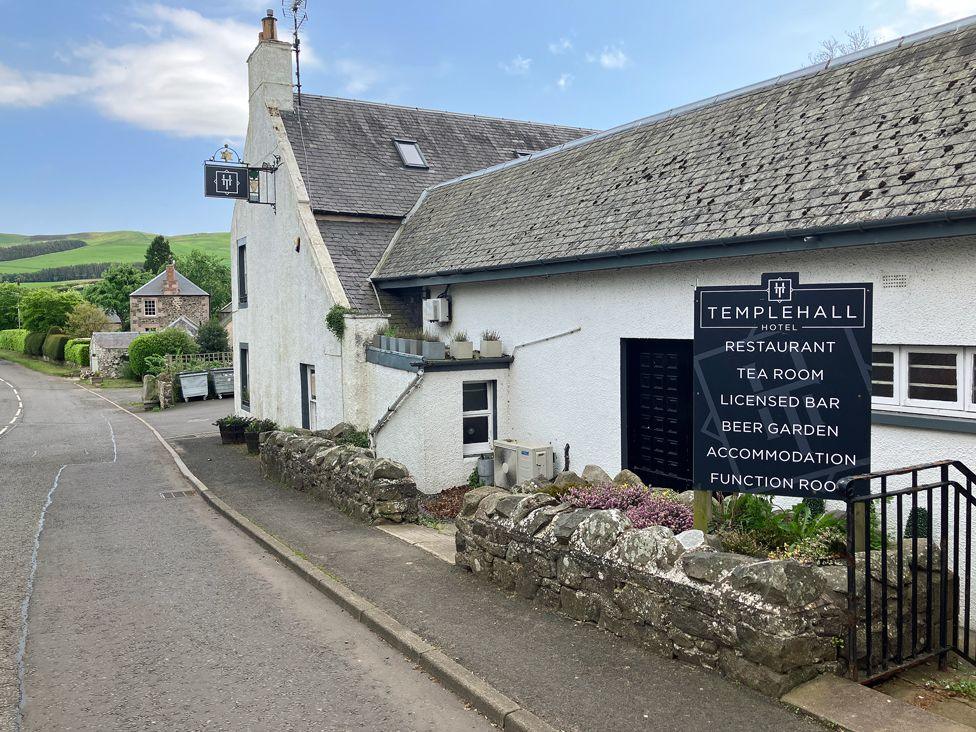 A white-walled village hotel and pub in the Scottish Borders with a sign outside advertising its facilities