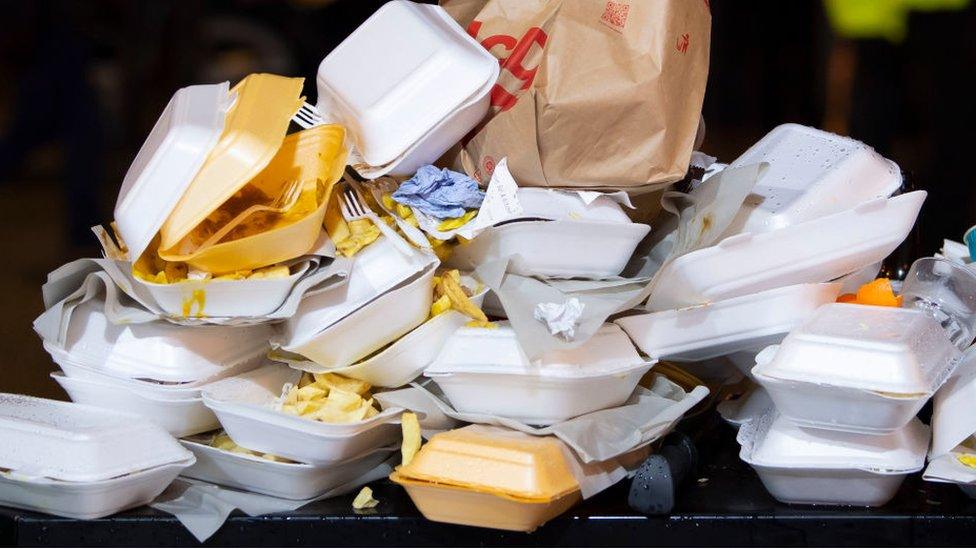 An overflowing bin full of takeaway food containers at nigh