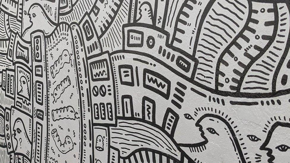 Black and white mural showing stylised people, patterns and structures