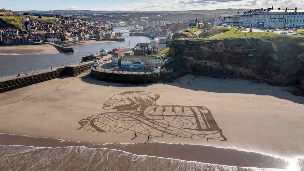 A giant sand portrait by WaterAid and artists Sand In Your Eye of Ansha, a 12-year-old from Frat in Ethiopia adorns Whitby Beach on March 15, 2021 in Whitby, England. Ahead of World Water Day on 22 March WaterAid created the portrait in the sand on Whitby Beach of a child carrying water next to the rising tide, to highlight the impact climate change is having on people’s access to water. The 60-metre wide artwork depicts Ansha from Frat in Ethiopia, who spends hours each day walking to and collecting dirty water from a river. After only an hour Ansha’s image was washed away by the rising tide – highlighting how excess rainfall and rising sea levels can lead to flooding, contaminating water and endangering lives.