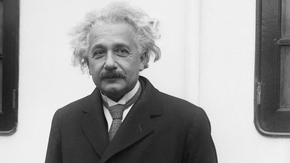 Albert Einstein standing on a ship wearing a coat and shirt and tie