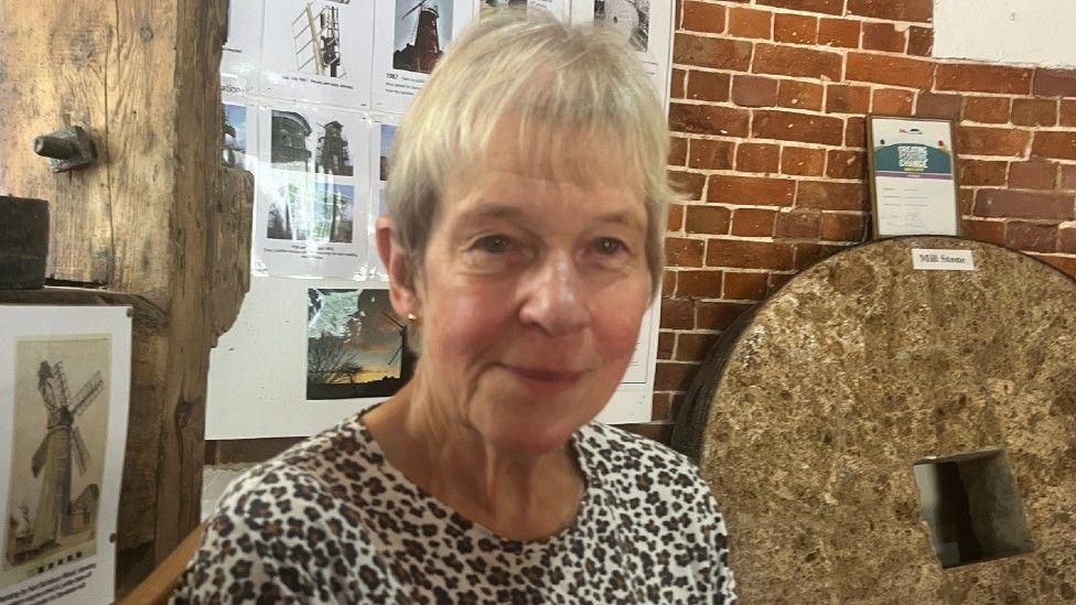 Philippa Whittington a lady with short blonde hair. She is sitting inside the windmill and is wearing a beige and brown leopard print T-shirt.