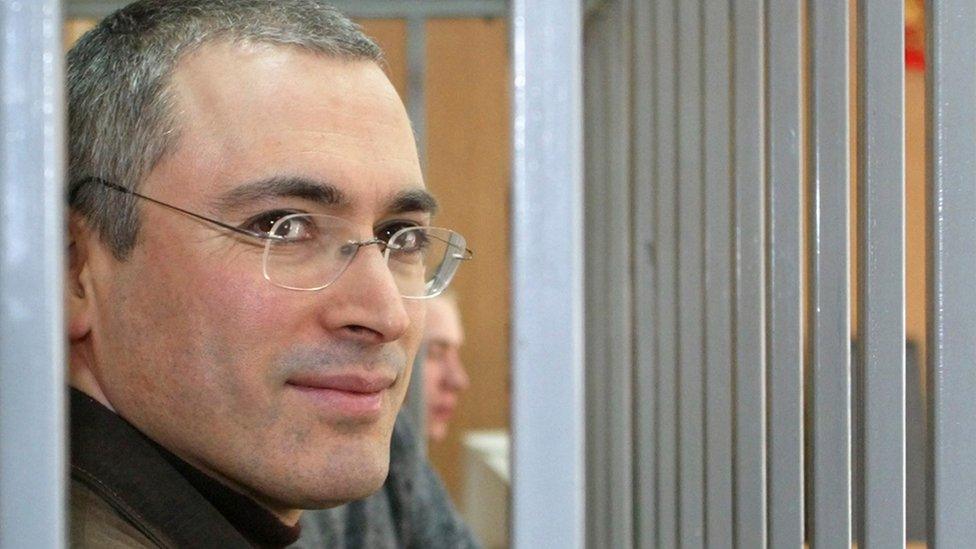 Former CEO of Russian oil gaint Yukos Mikhail Khodorkovsky smiles from behind bars, as he listens to a prosecutor during his trial in Moscow, Monday, March 28, 2005.