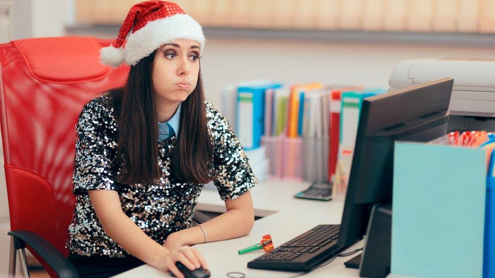 Woman wearing Santa hat looks exasperated at her desk