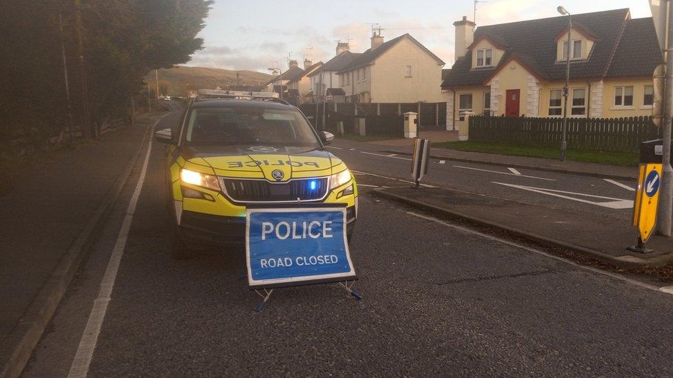 Police car behind sign reading "POLICE ROAD CLOSED"