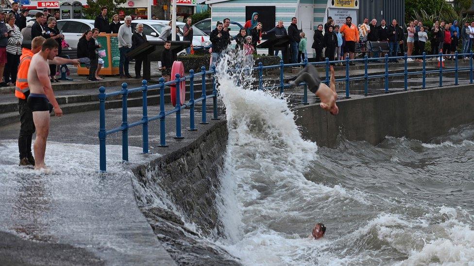 A man jumps in the sea at Saundersfoot as another in the water watches on, and another in boxer shorts watches from the seafront