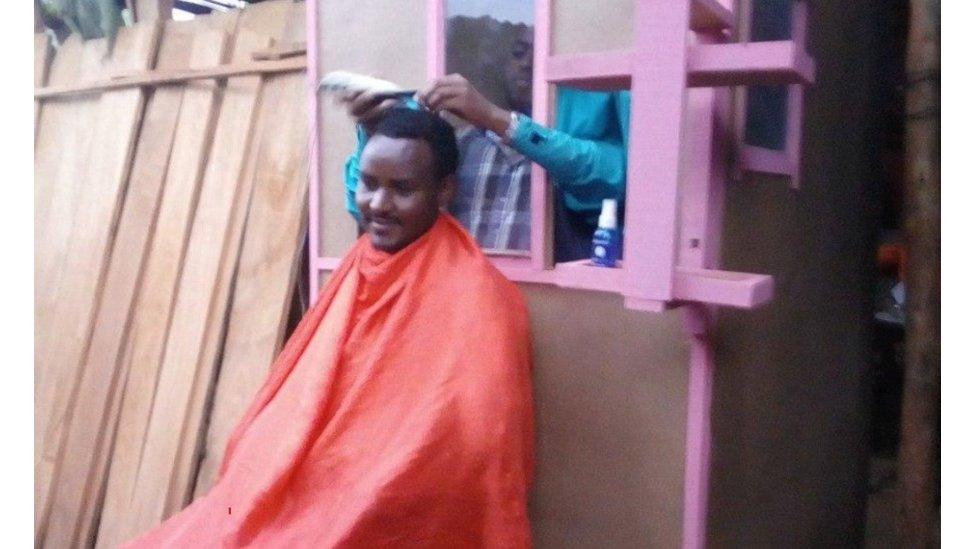 Man getting a haircut with hairdresser behind a wooden shield