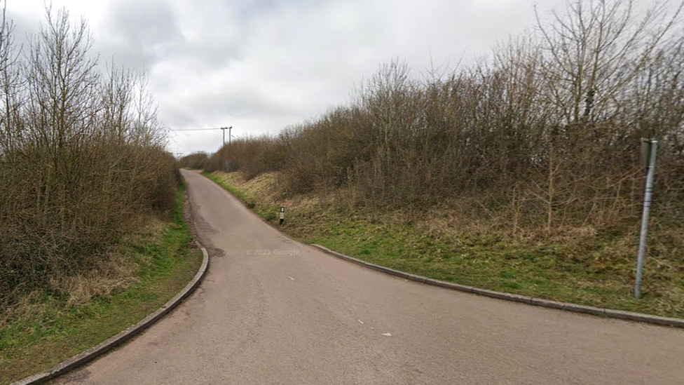 The entrance to Rock Road in Wick showing hedges either side of a single-track road