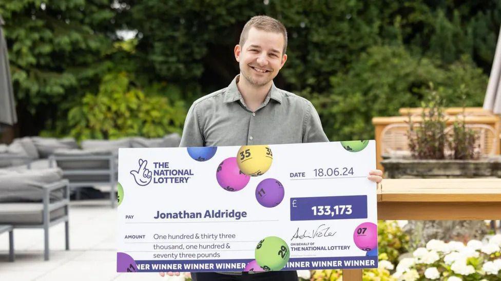 Jonathan Aldridge holds his winning cheque