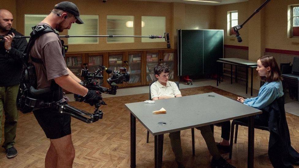 Cameraman Matthew Lewi films actors Owen Cooper and Erin Doherty in a child psychology room on the set of Adolescence