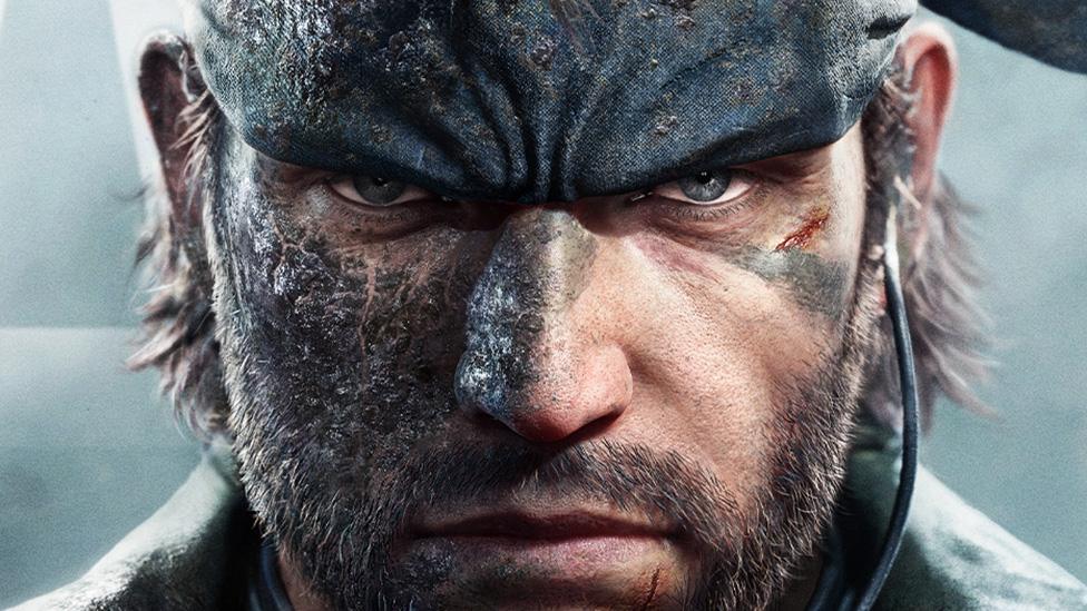 Metal Gear Solid hero Snake looks ready for action. His eyes are narrowed, focusing intently on the viewer, and his famous bandana is visible around his head. One side of his face is caked in mud and he has a small, fresh cut under his left eye.