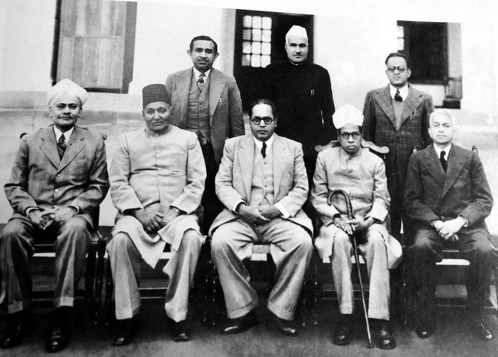 On 30 August 1947, the seven-member Drafting Committee of the Constituent Assembly met and unanimously elected Ambedkar as chairman. Barring him and Muhammad Saadulla, a lawyer from Assam, all the members were Savarnas. With Ambedkar (seated from the left) are three other members of the Committee, N. Madhavrao, Muhammad Saadulla and Alladi Krishnaswami Aiyar, and constitutional adviser B.N. Rau. Standing: S.N. Mukherjee, Jugal Kishore Khanna and Kewal Krishan (administrative officers).