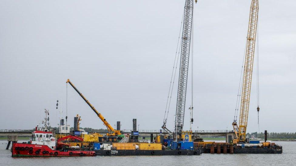 A tug boat and cranes are seen at the construction site of the Uniper Liquefied Natural Gas (LNG) terminal at the Jade Bight in Wilhelmshaven on the North Sea coast, north-western Germany, on September 29, 2022