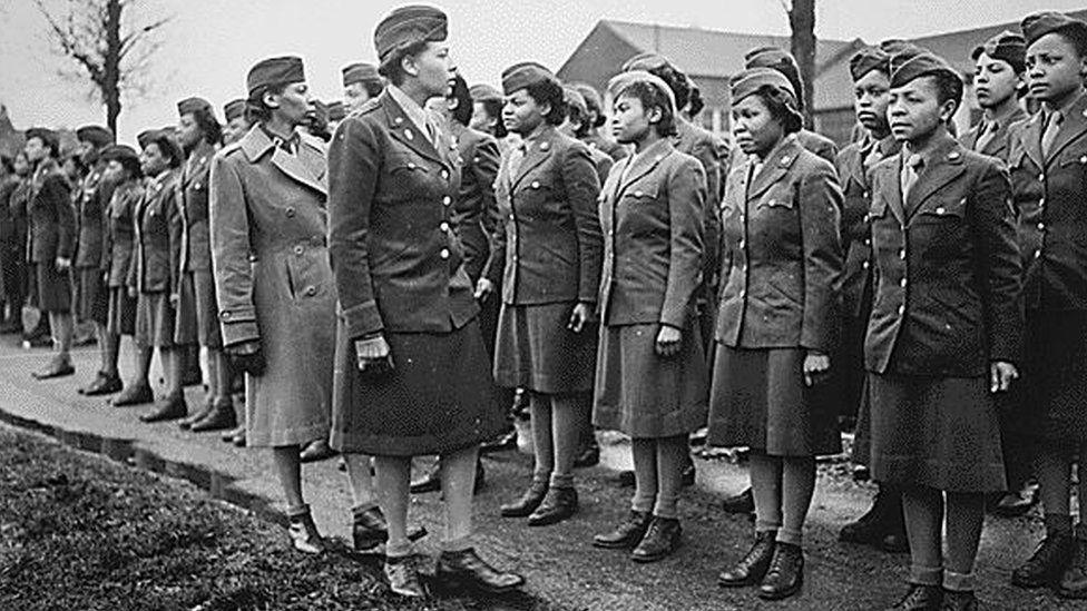 A black and white image showing Maj Charity Adams reviewing her troops. She is walking up a double line of women US Women's Army Corps uniform, and they are standing at attention. 1945 or 1946