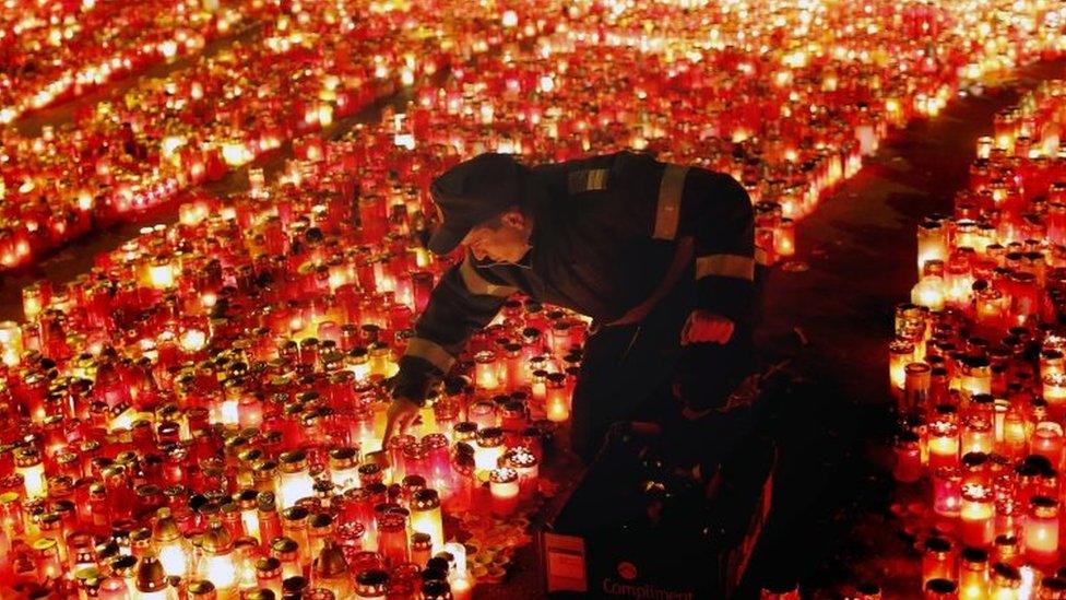 A Romanian policeman arranges burning candles placed at the scene of the fire by people paying their respects for the victims (02 November 2015)