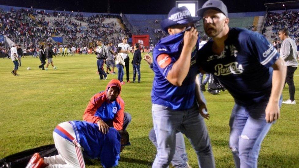 Spectators react from tear gas after riotsing breaks out at the National Stadium in Tegucigalpa, 17 August