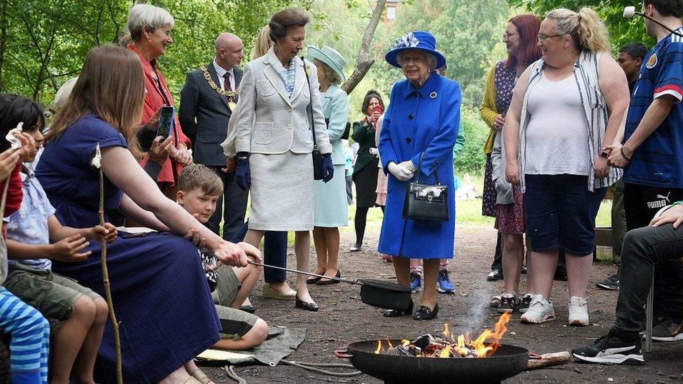 The Queen and Princess Anne stand in front of fire