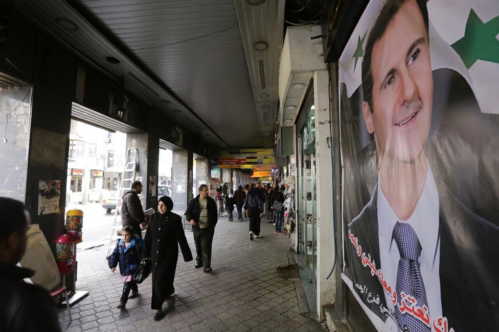 Syrians walk past poster of Bashar al-Assad