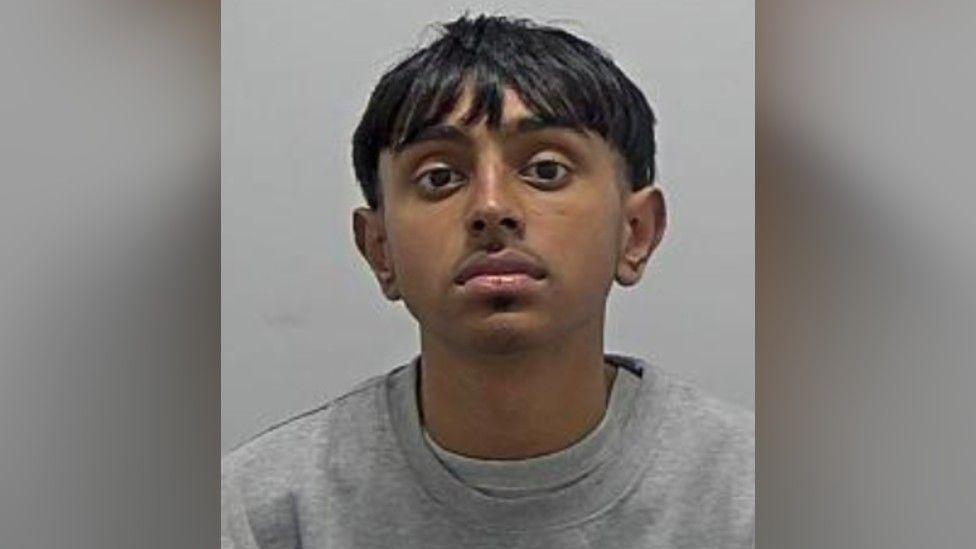 Riaz Miah: The head and shoulders of a man with straight black hair, and black moustache. wearing a grey. round-necked top.