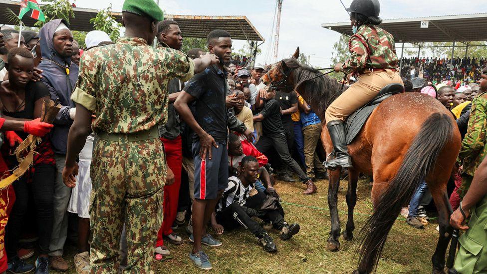An officer on horseback and another officer - both with their backs to the camera - try to control the crowd at a stadium in Kisumu.