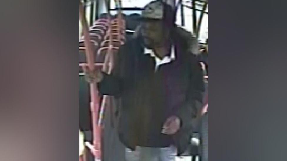 A man wearing a dark coat and a black and white cap standing on a bus