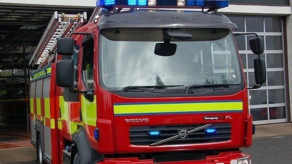 A red and yellow fire engine with its blue lights on exiting a fire station.