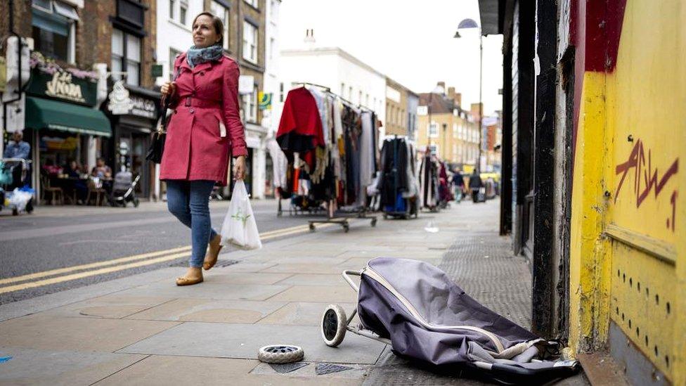 A woman walks past a broken shopping trolley at Petticoat Lane Market in London, UK, on 12 October 2022