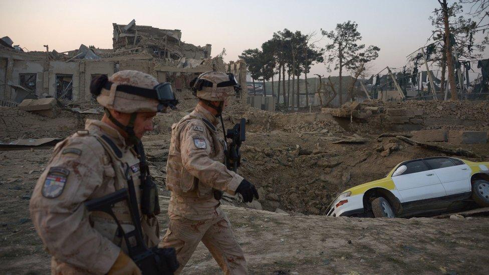 Croatian soldiers from the NATO coalition are walking past a crater from a bomb blast as they inspect the site of an attack targeting the German consulate in Mazar-i-Sharif on November 11, 2016.