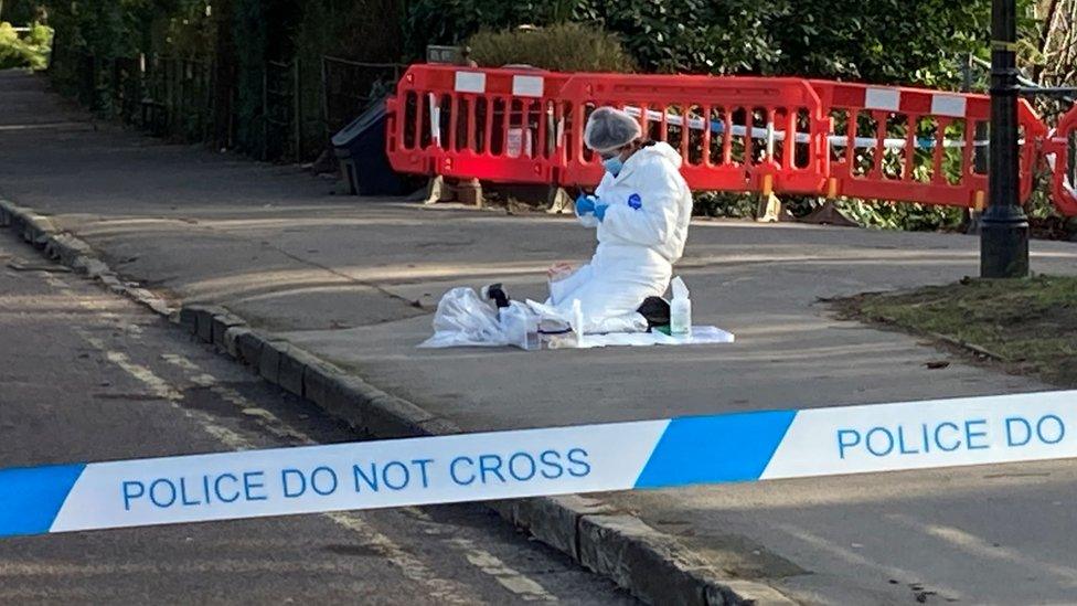 An investigator in white outfit kneeling on the floor behind police tape