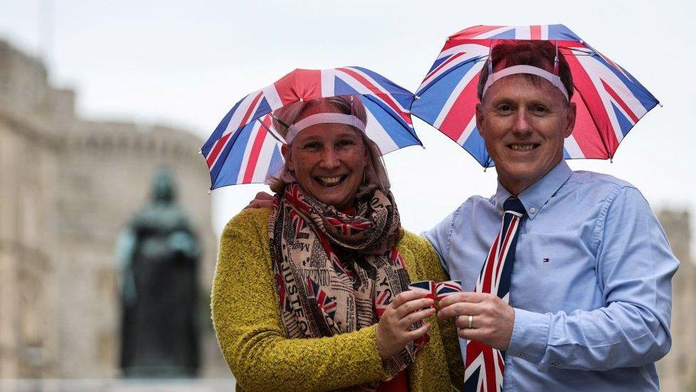 A man and a woman wear umbrella hats with the flag of England