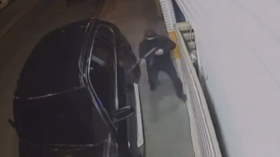 A gunman wielding a rifle approaches a black car