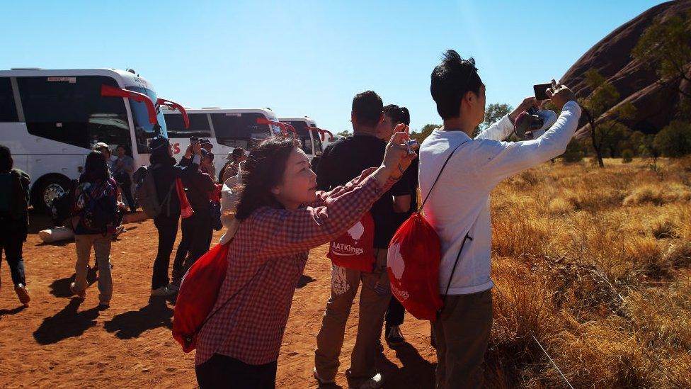 Visitors take photos from the base walk area at Uluru on August 12, 2019